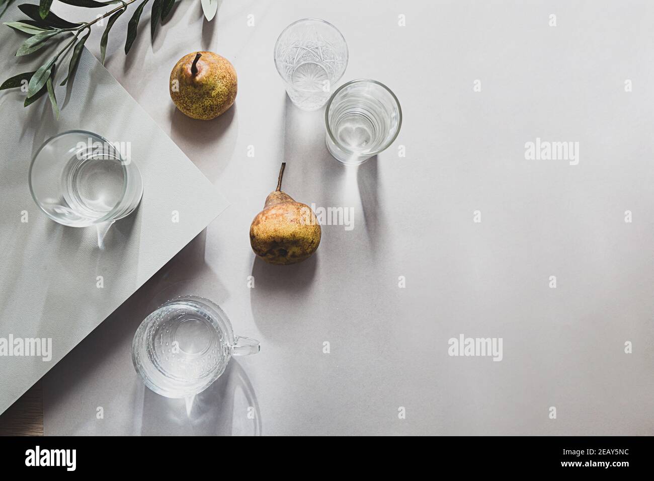 Still life minimalista di pere e bicchieri d'acqua vista dall'alto. Composizione estiva luce e ombra su un tavolo grigio Foto Stock
