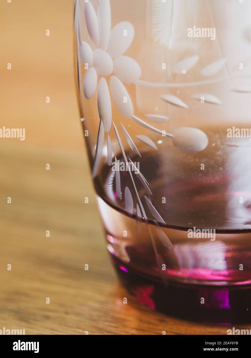 Un bicchiere d'annata, disegno di fiori incisi, vino rosso porpora rosa  colorato, con una piccola quantità di acqua in esso su un tavolo di legno  Foto stock - Alamy