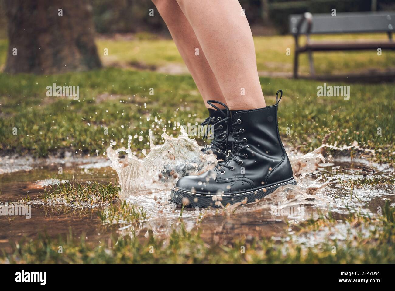 Fuoco selettivo di una donna che indossa stivaletti neri saltando su una pozza in un parco Foto Stock