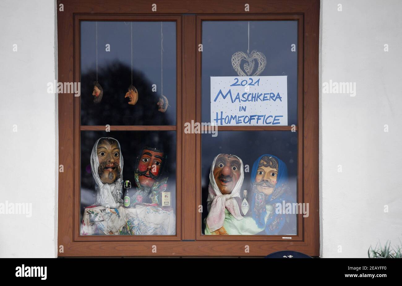 Farchant, Germania. 11 Feb 2021. In una finestra si possono vedere larve di legno, che la gente del posto indossa di solito durante la tradizionale passeggiata Maschkera, e un segno con l'iscrizione '2021 Maschkera nell'ufficio di casa'. Quest'anno, streghe, gnomi, campanili e altri personaggi del carnevale sono anche a casa - e così in Farchant in alta Baviera, figure con maschere storiche accolgono i visitatori dalle finestre o balconi. Credit: Angelika Warmuth/dpa/Alamy Live News Foto Stock