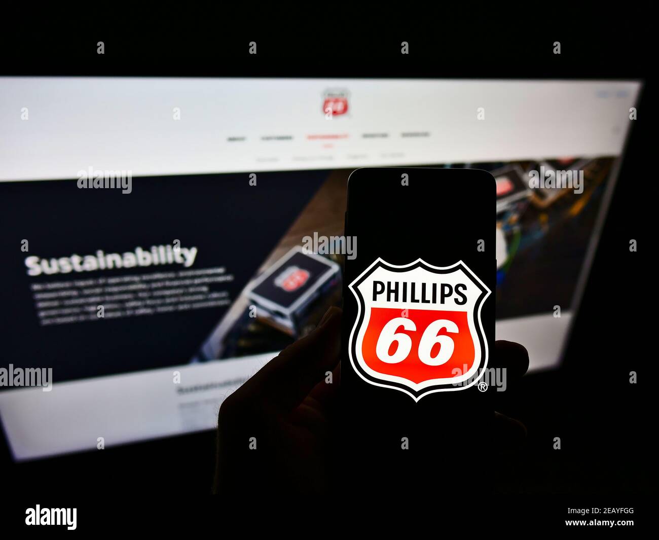Persona che tiene il cellulare con il logo del commercio americano del petrolio e del gas Phillips 66 Company sullo schermo davanti al Web site di affari. Focus sul display del cellulare. Foto Stock