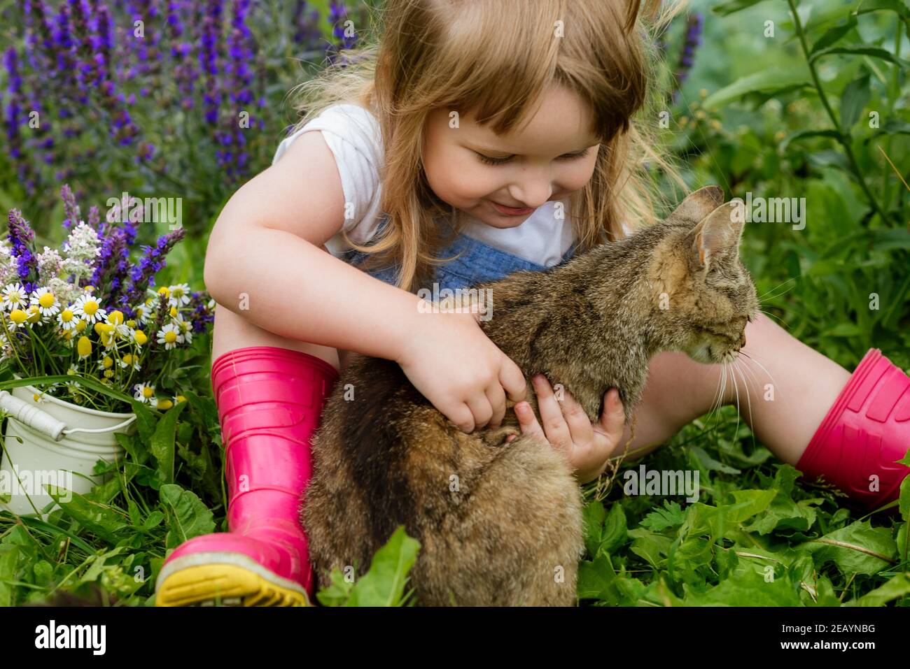 Bambino felice con gatto. Ragazza che gioca con l'animale domestico all'aperto in giardino. Natura estiva Foto Stock