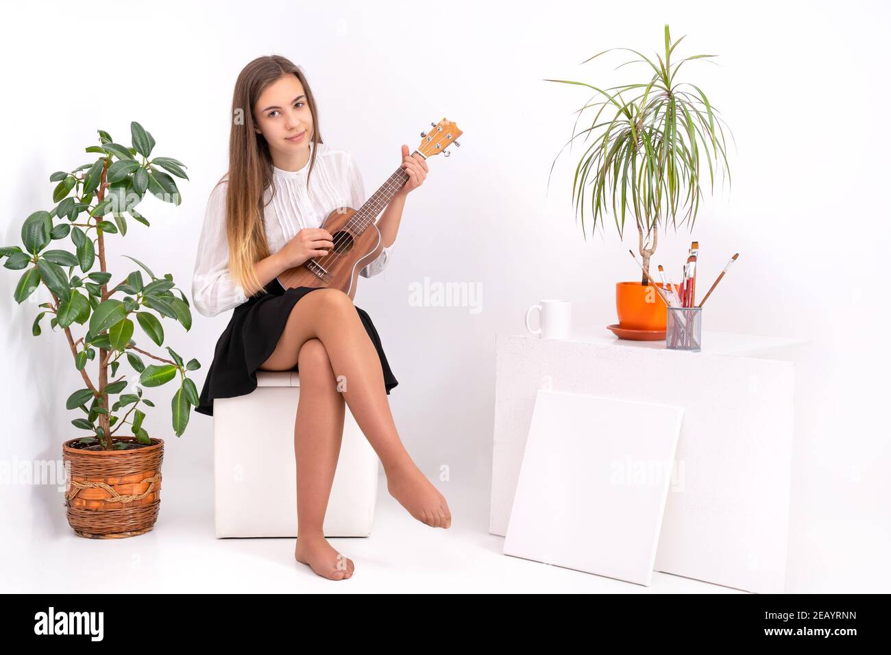 Bella giovane signora in uno studio d'arte che gioca l'ukulele indossando una blusa bianca e una gonna nera Foto Stock
