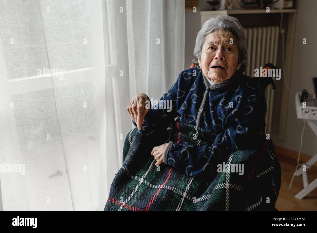 Ritratto vecchia donna malata seduta in sedia a rotelle a casa con volto confuso. Terza età, concetto di assistenza per anziani domestici. Foto Stock