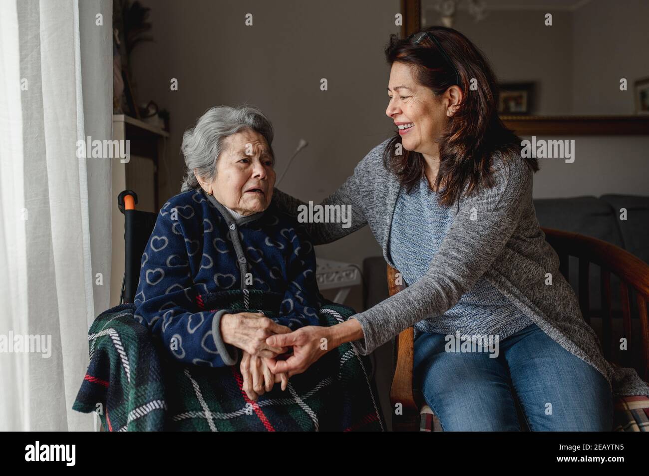 Vecchia donna malata in sedia a rotelle accanto alla figlia sorridente. Terza età, concetto di cura domestica. Foto Stock