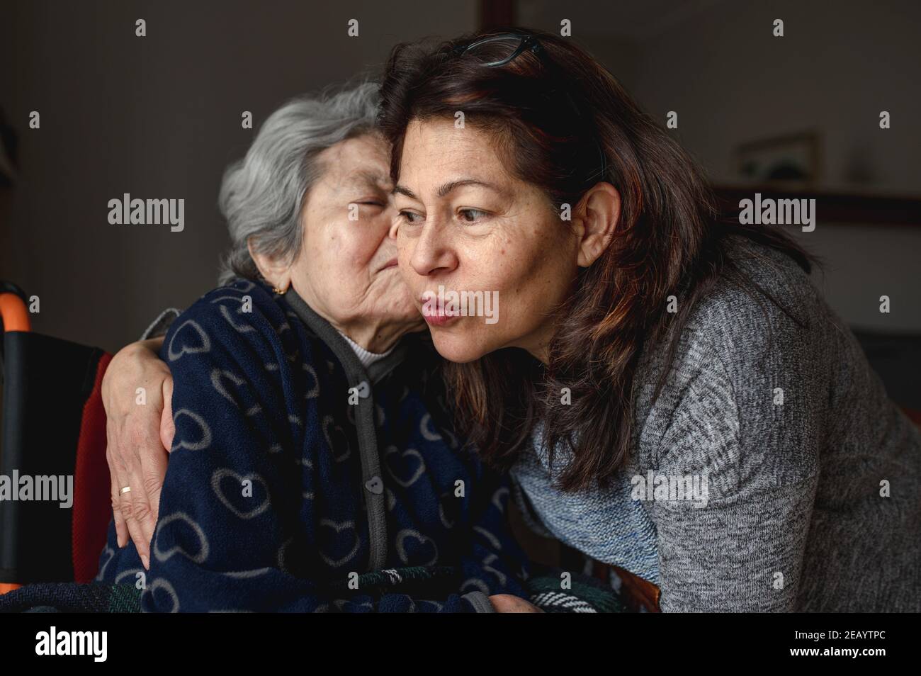 Donna anziana malata in sedia a rotelle che bacia la figlia. Terza età, concetto di cura domestica. Foto Stock
