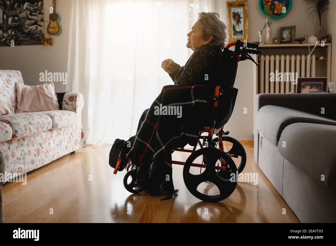 Donna anziana malata in sedia a rotelle nel mezzo della casa camera da sola Foto Stock