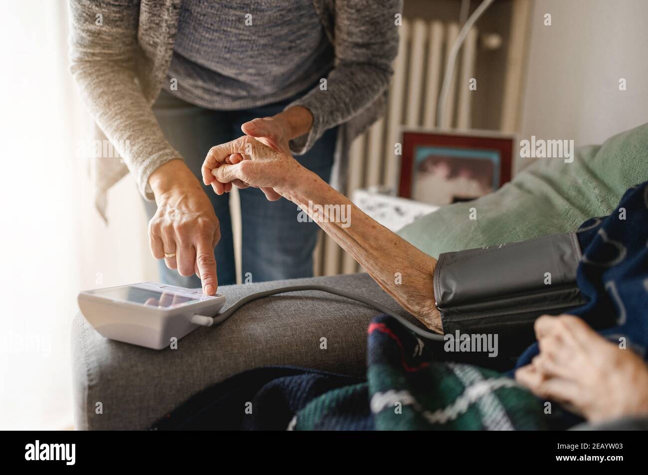 Donna irriconoscibile che misura la tensione con il tensiometro ad una persona anziana. Assistenza e assistenza domiciliare, concetto di anziani. Foto Stock