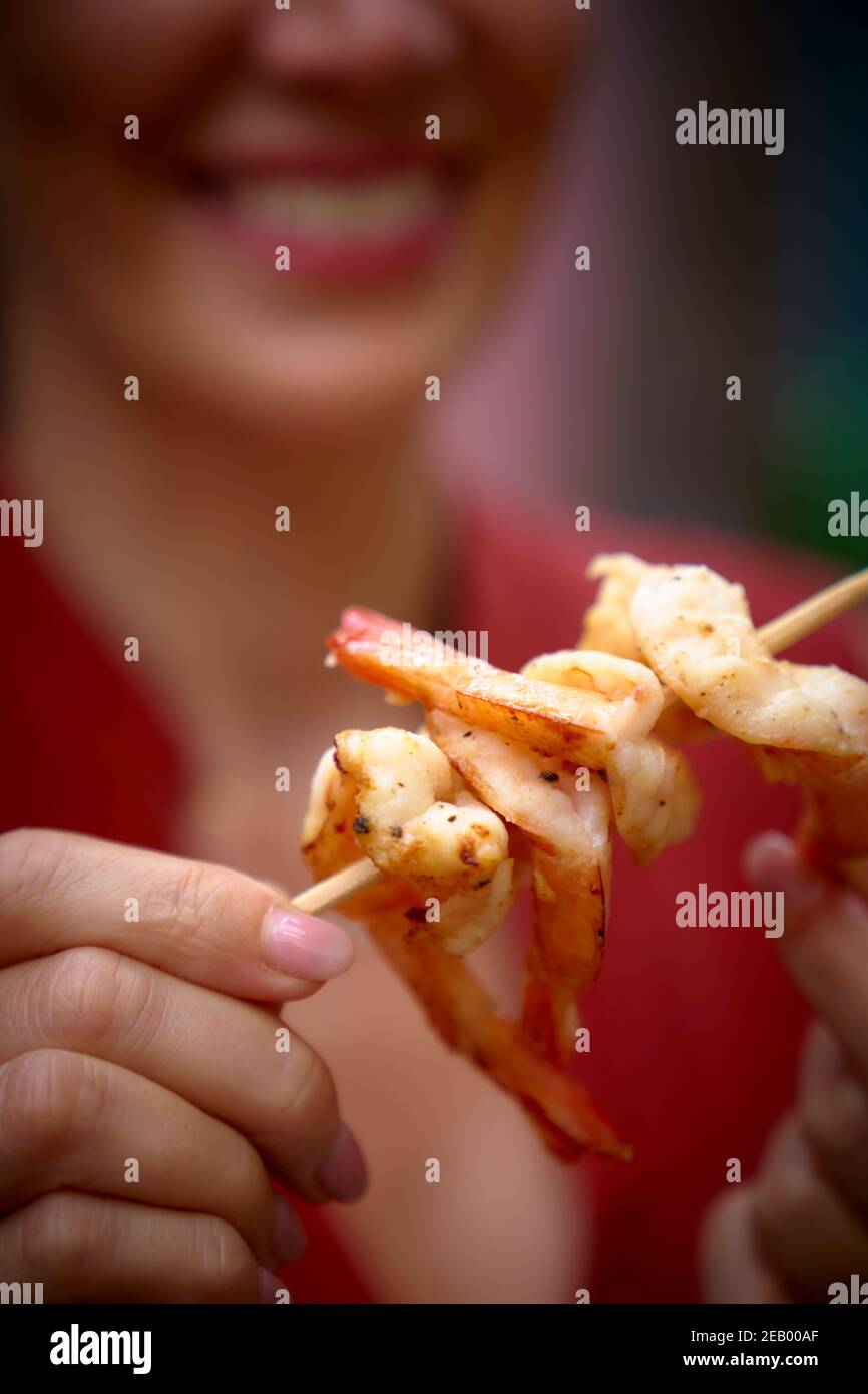 Cibo di strada asiatico, gamberi su uno spiedino tenuto da una donna Foto Stock