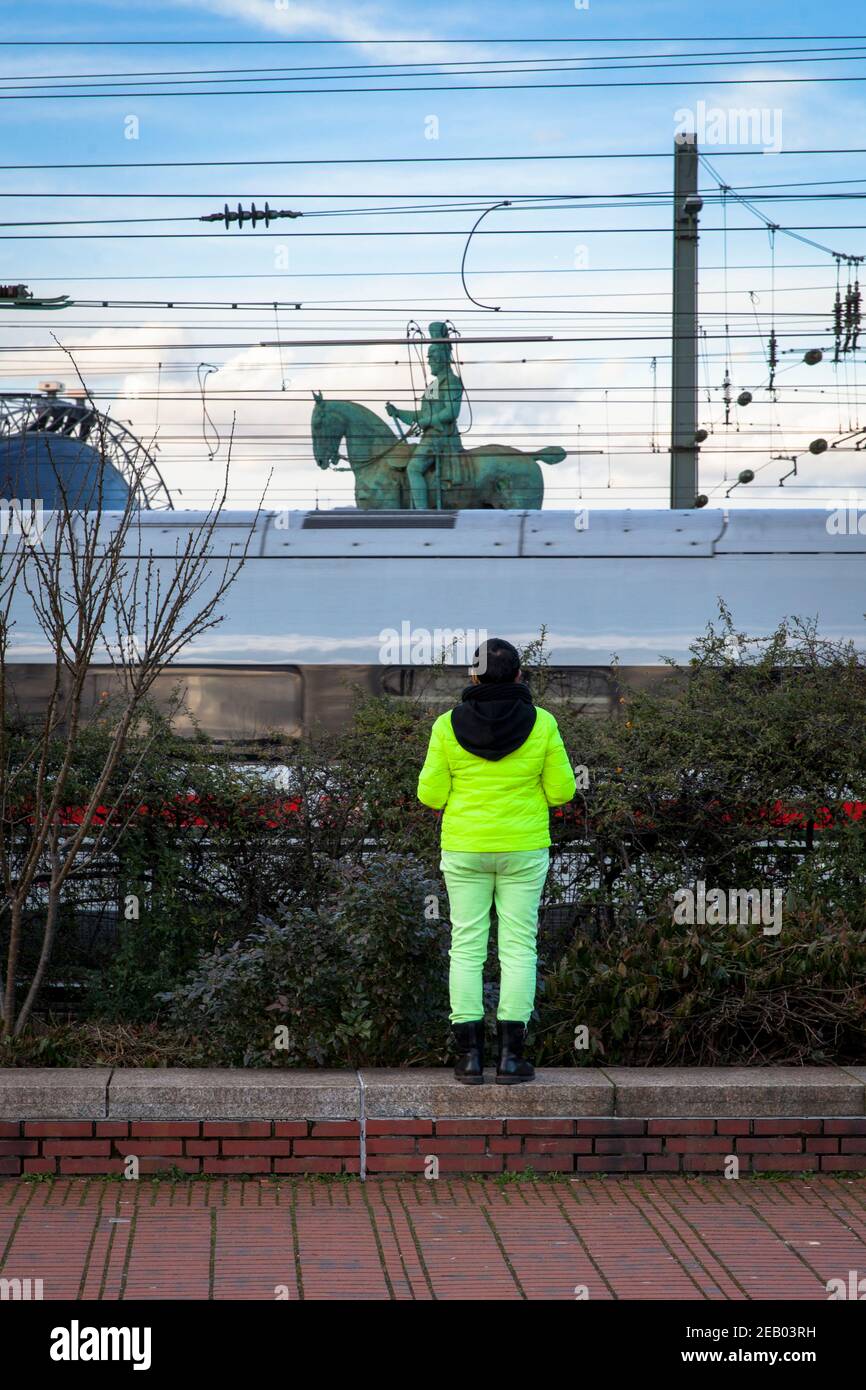 Donna in piedi vicino alla linea ferroviaria vicino al ponte di Hohenzollern guardando verso il monumento equestre, treno mobile, Colonia, Germania. Frau steht Foto Stock