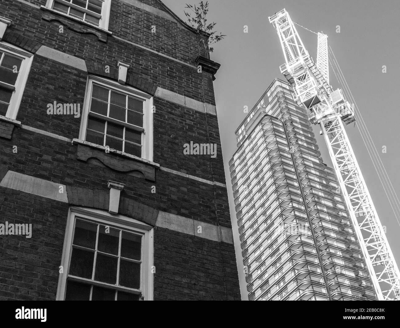 Un alto e moderno isolato a torre residenziale e una gru a torre si ergono accanto ad un edificio molto più vecchio in Blossom Street, Shoreditch, Londra Foto Stock
