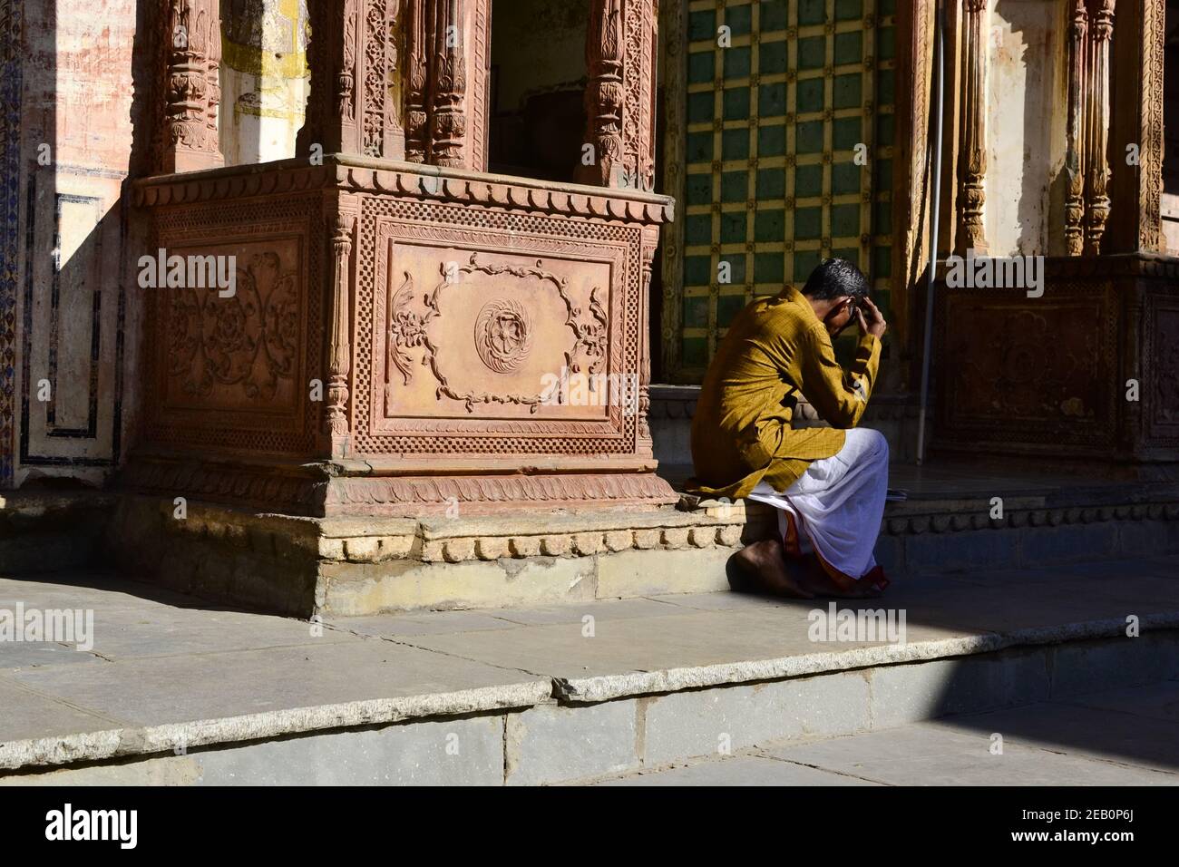 Pushkar, Rajasthan, India - Dicembre 2016: Uomo indiano seduto sul pavimento e legge giornale. Indù vicino al tempio con pareti decorative Foto Stock