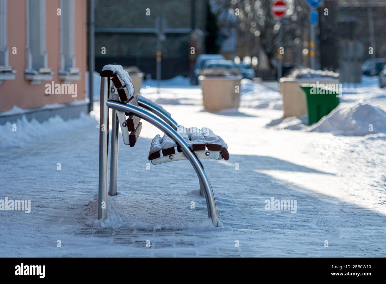 una panchina vuota e nevosa sul lato della strada su un marciapiede lastricato, vista laterale, primo piano Foto Stock