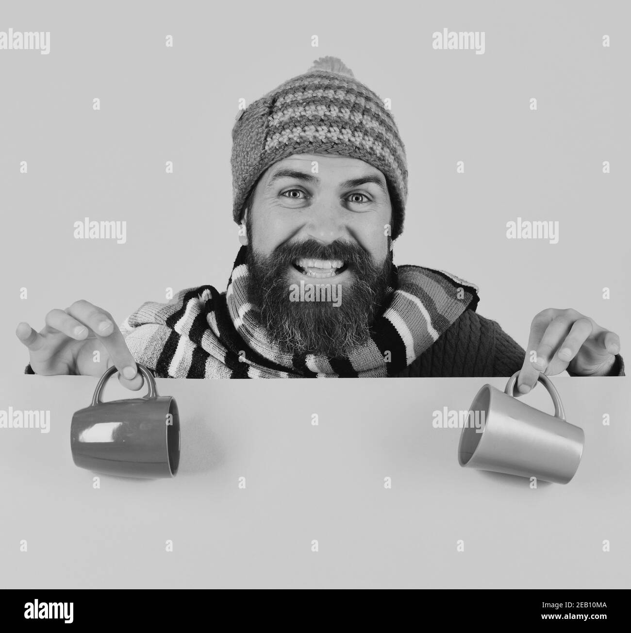 Mattina d'autunno perfetta e concetto di aroma. Idea dell'ora della colazione. L'uomo in cappello caldo tiene una tazza marrone e verde su sfondo rosa, spazio copia. Hipster con barba e happy face ha una tazza di caffè. Foto Stock