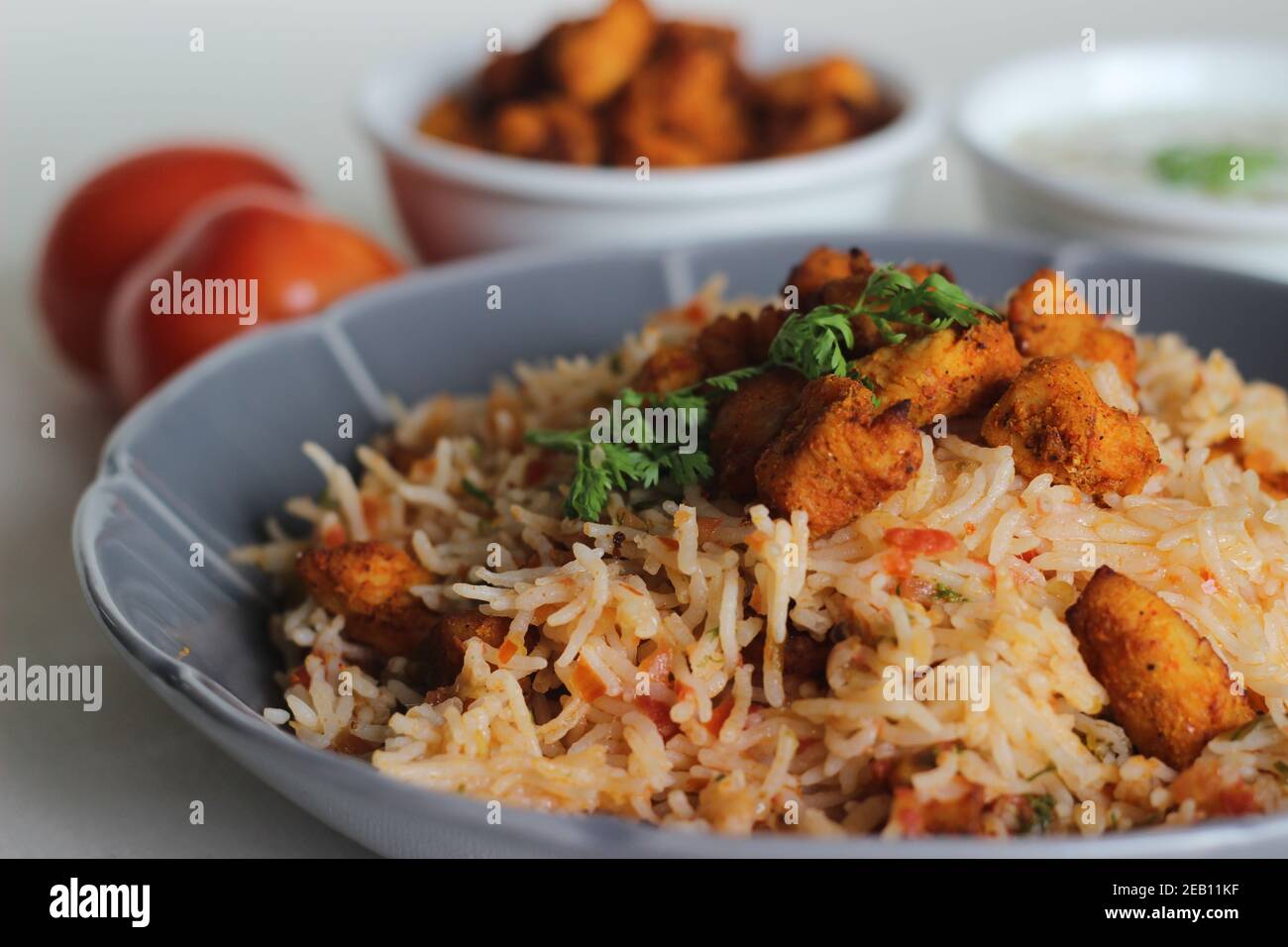 Riso al pomodoro servito con raita e bocconcini di pollo disossati fritti all'aria. Scatto su sfondo bianco. Servito su una ciotola grigia Foto Stock
