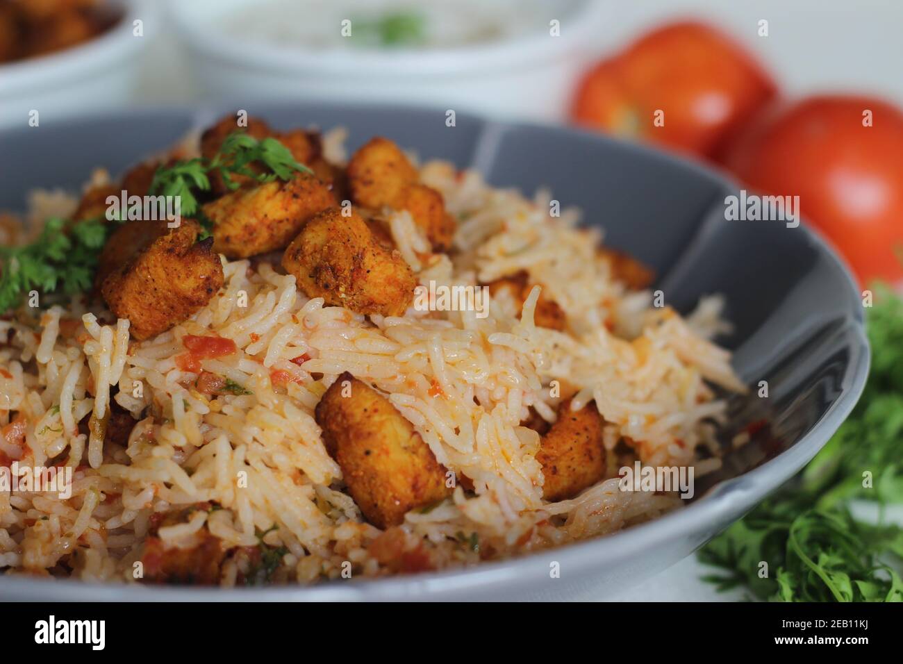 Riso al pomodoro servito con raita e bocconcini di pollo disossati fritti all'aria. Scatto su sfondo bianco. Servito su una ciotola grigia Foto Stock