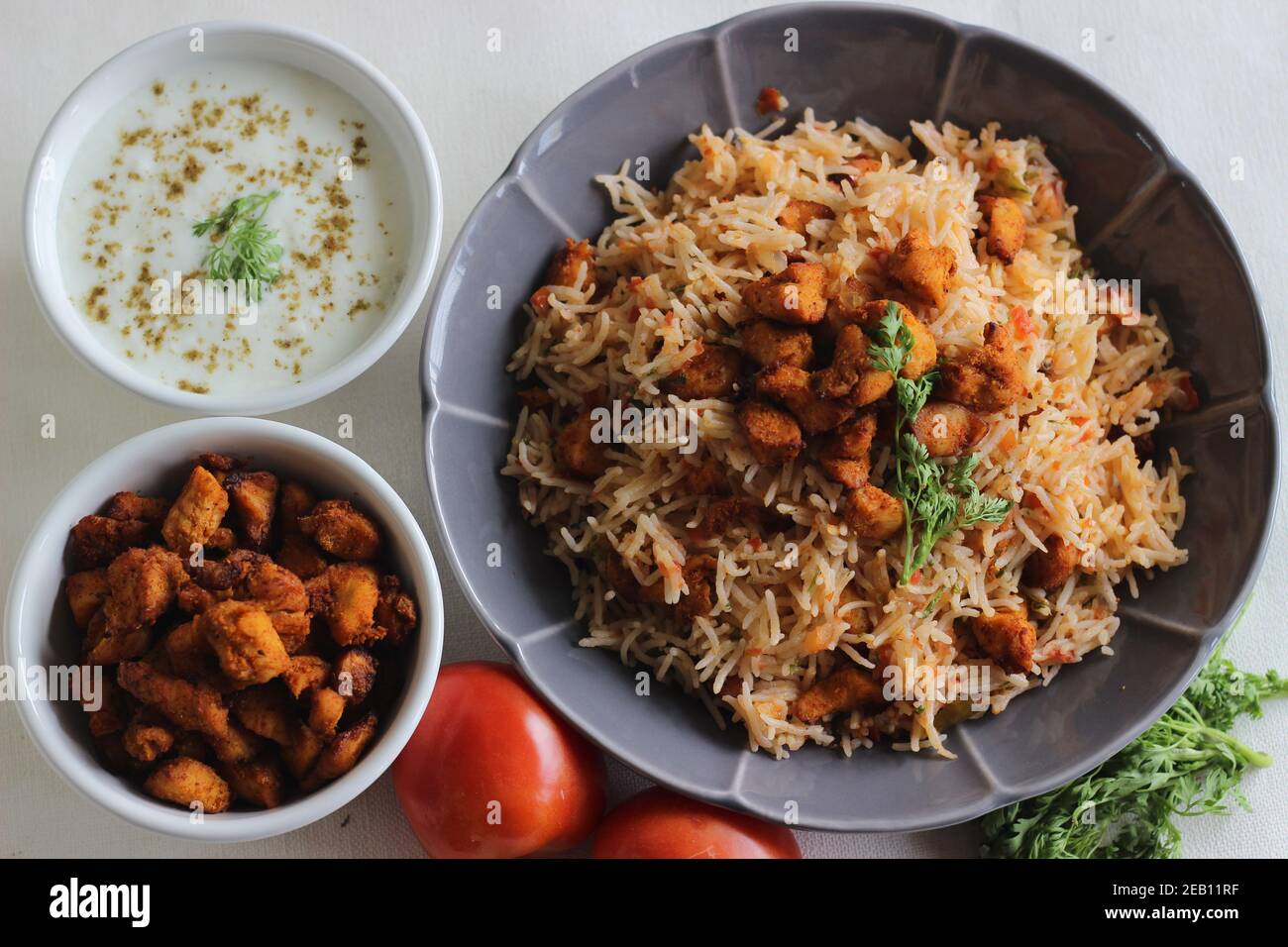 Riso al pomodoro servito con raita e bocconcini di pollo disossati fritti all'aria. Scatto su sfondo bianco. Servito su una ciotola grigia Foto Stock