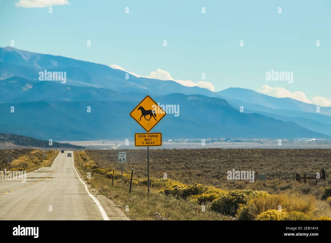 Un termoeffetto sulla strada e le vetture nel alto deserto con montagne in lontananza e un cartello Con un cavallo che dice Open Range Foto Stock