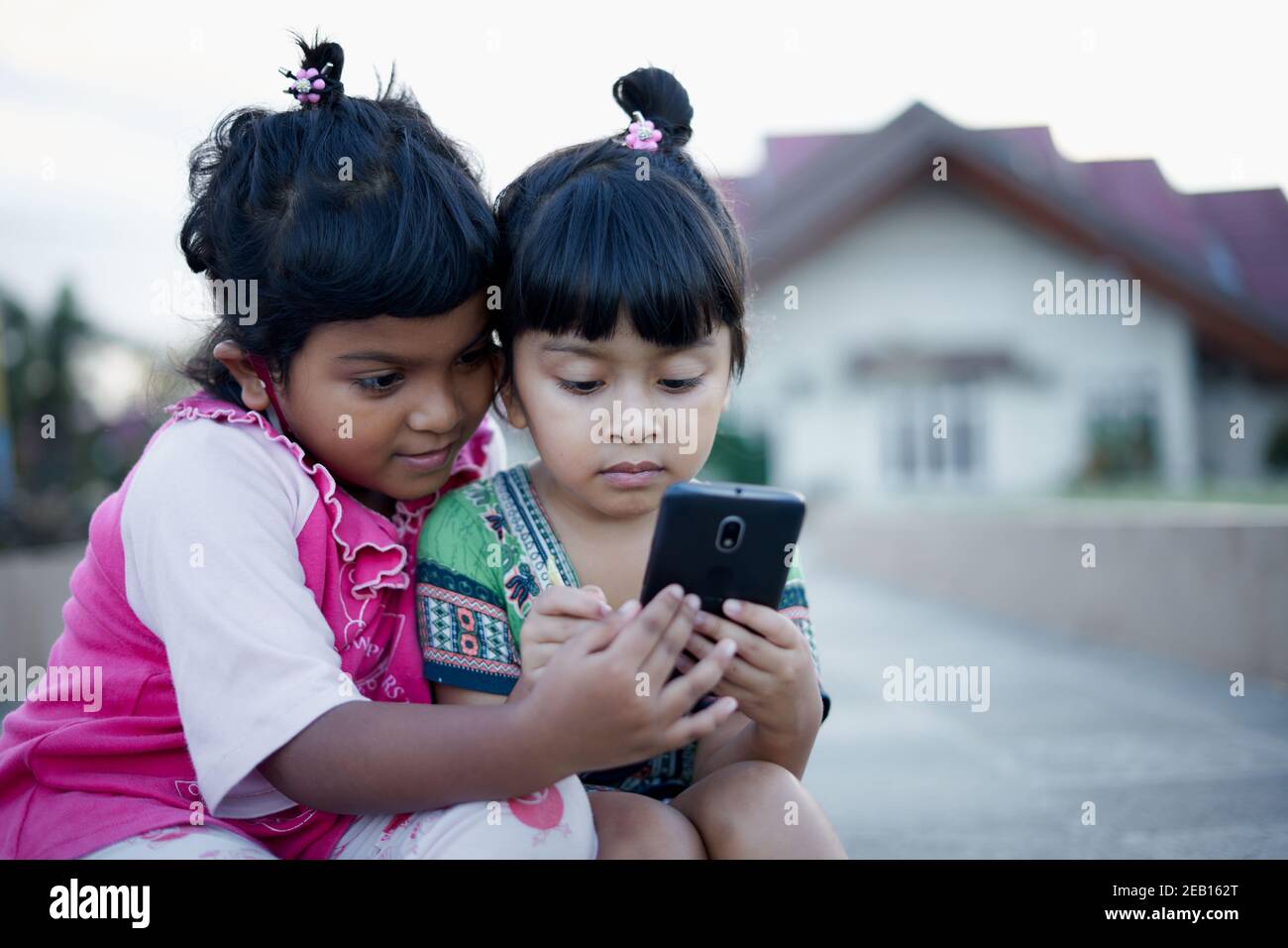 Due bambine giocano e imparano con il loro smartphone nel parco pubblico. Bambini e tecnologia in pandemia nuovo concetto normale Foto Stock