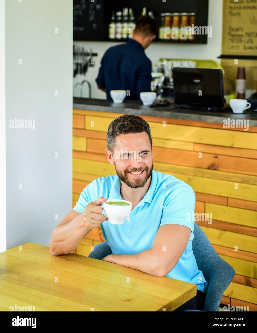 Uomo sopportato ragazzo bevande cappuccino tavolo caffè in legno. Il visitatore del Cafe, felice faccia sorridente, gustatevi una bevanda a base di caffe'. Migliorare la salute generale. Prendetevi il momento di prendervi cura di voi stessi. I bevitori di caffè vivono più a lungo. Foto Stock