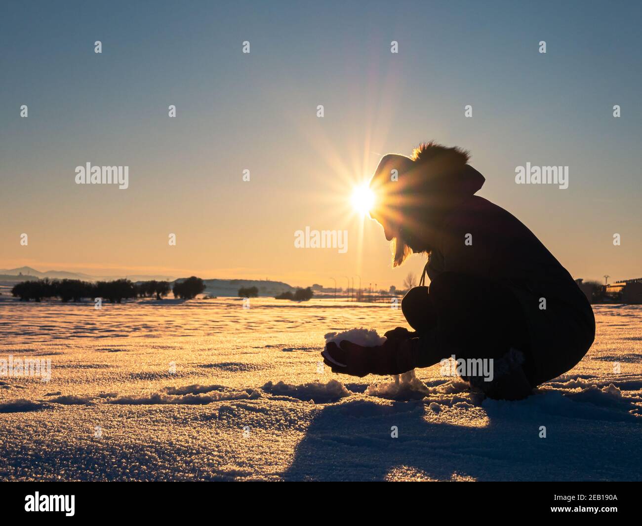 bella foto di una donna accovacciata giù raccogliendo la neve dentro un bellissimo campo di neve al tramonto Foto Stock