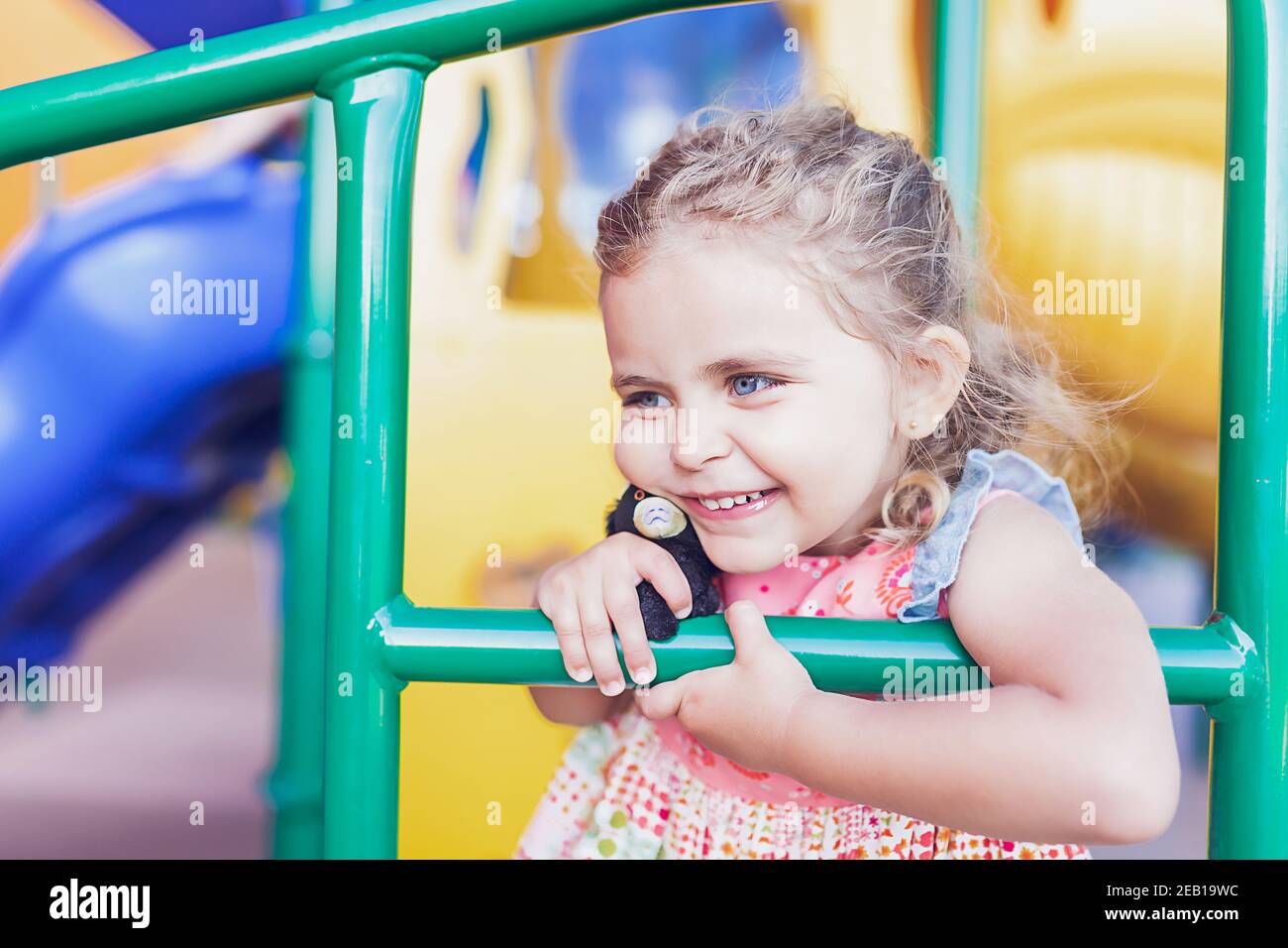 Ragazza preschooler che tiene un orsacchiotto che gioca in un parco giochi pubblico. Foto Stock