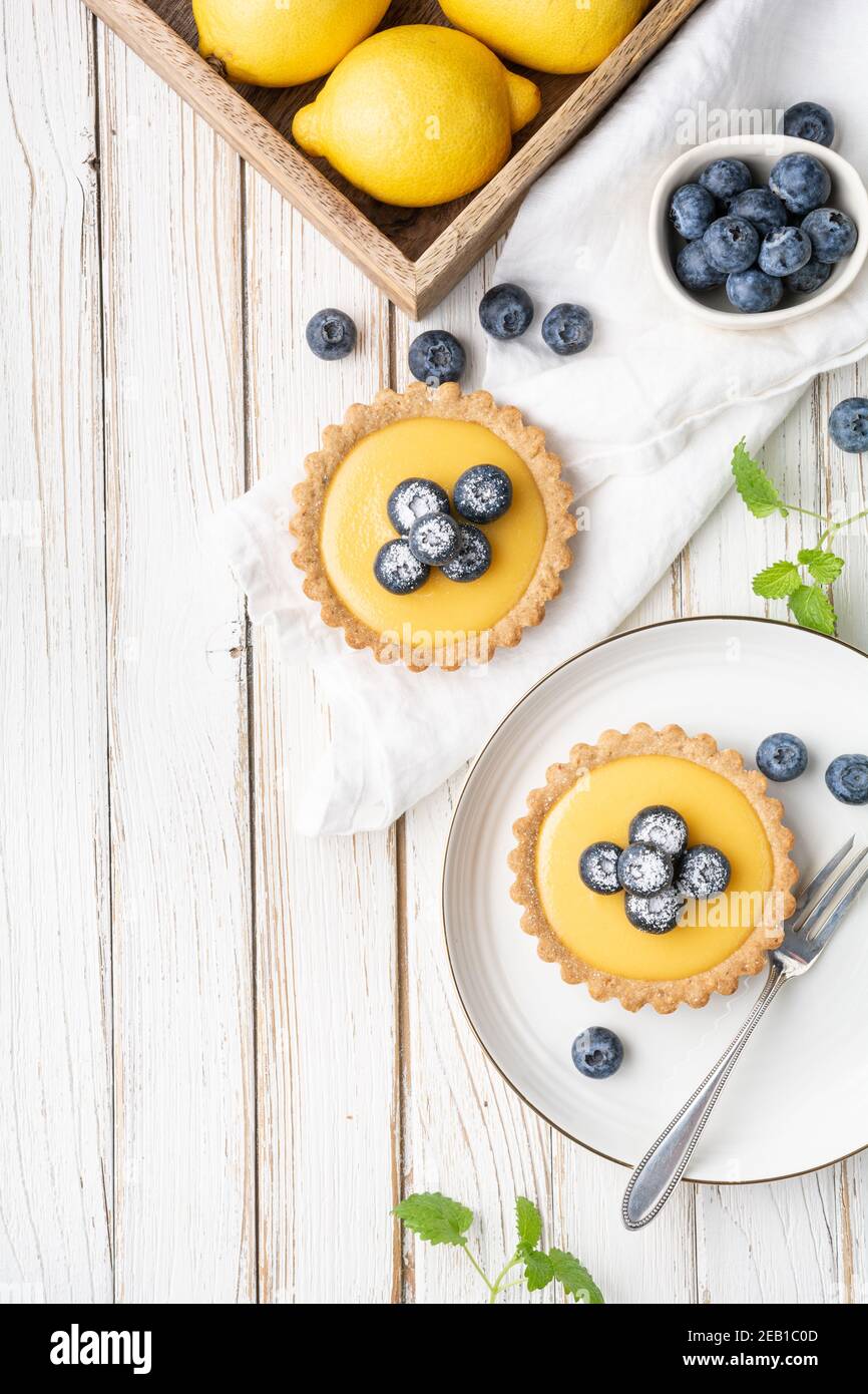 Tartlet di crosta di noce con ripieno di cagliata di limone, ricoperta di mirtilli freschi e cosparsa di zucchero in polvere su rustico fondo di legno Foto Stock