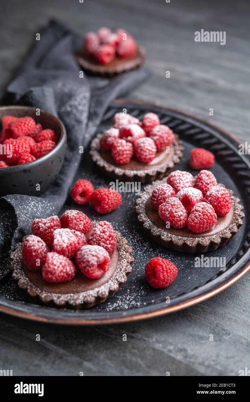 Tartine di crosta di cacao ripieni di mousse al cioccolato fondente fatta di panna montata e purea di lamponi, condite con frutti di bosco freschi, cosparse di polvere Foto Stock