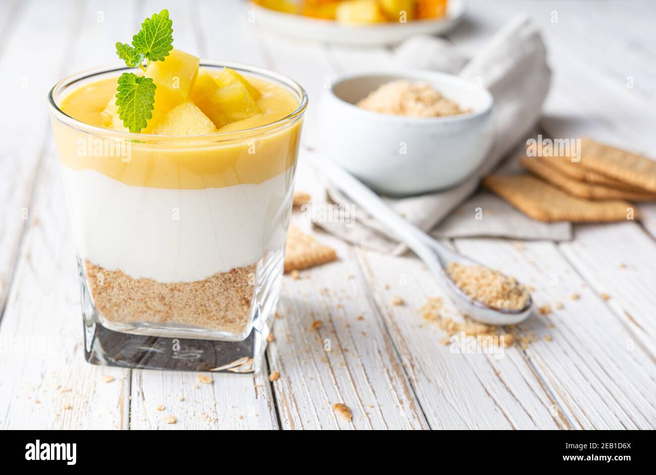 Dolce dessert a strati con cracker di graham schiacciati, formaggio cremoso e cagliata di ananas, condito con fette di frutta fresca in un vaso di vetro su vecchio dorso di legno Foto Stock