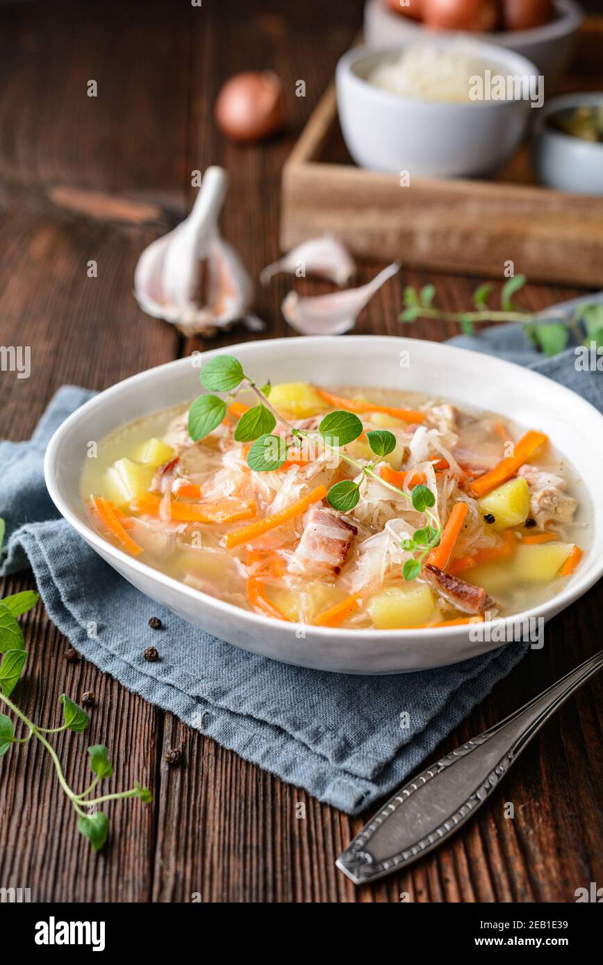 Kapusniak, zuppa polacca classica a base di crauti, costolette di maiale, pancetta affumicata, patate, carote e altre verdure in piastra di ceramica profonda su legno rustico Foto Stock