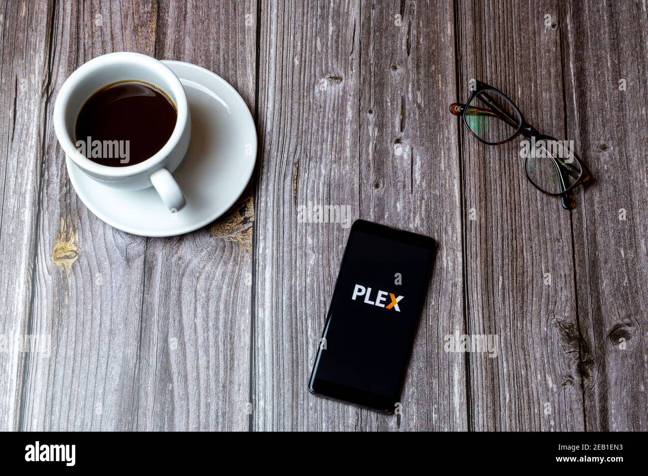 Un telefono cellulare o un telefono cellulare posato su un legno Tabella con l'app Plex aperta sullo schermo accanto a. un caffè Foto Stock