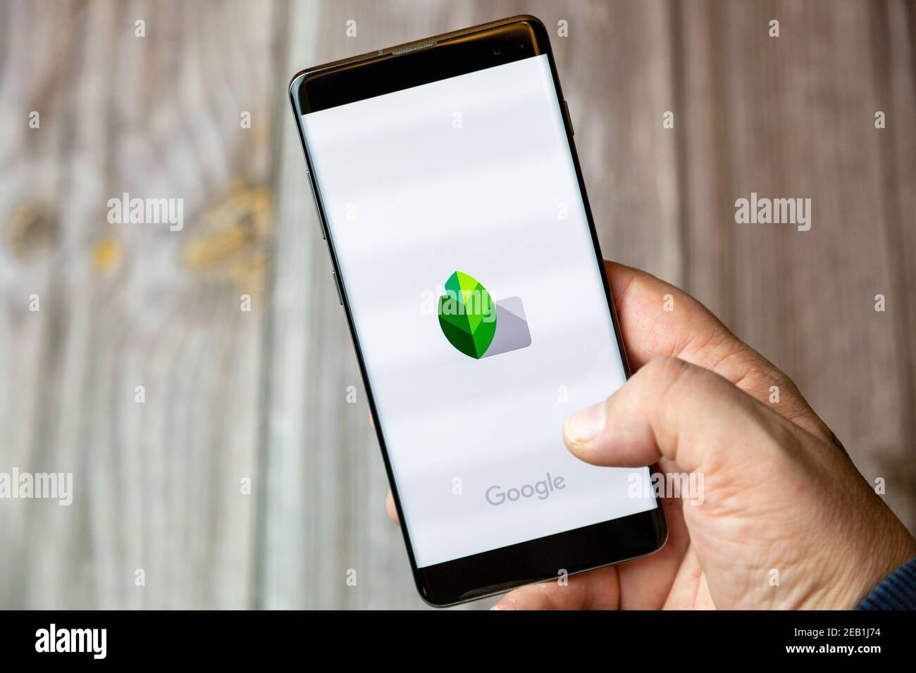 Un telefono cellulare o un telefono cellulare tenuto da un mano con l'app snapseed aperta sullo schermo Foto Stock