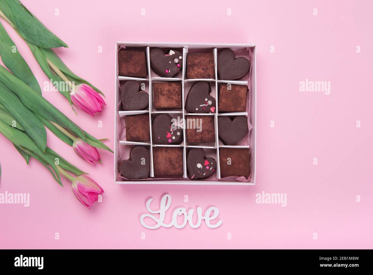 Confezione regalo con cuori di dolci al cioccolato e tulipani su sfondo rosa. Deserto per San Valentino Foto Stock