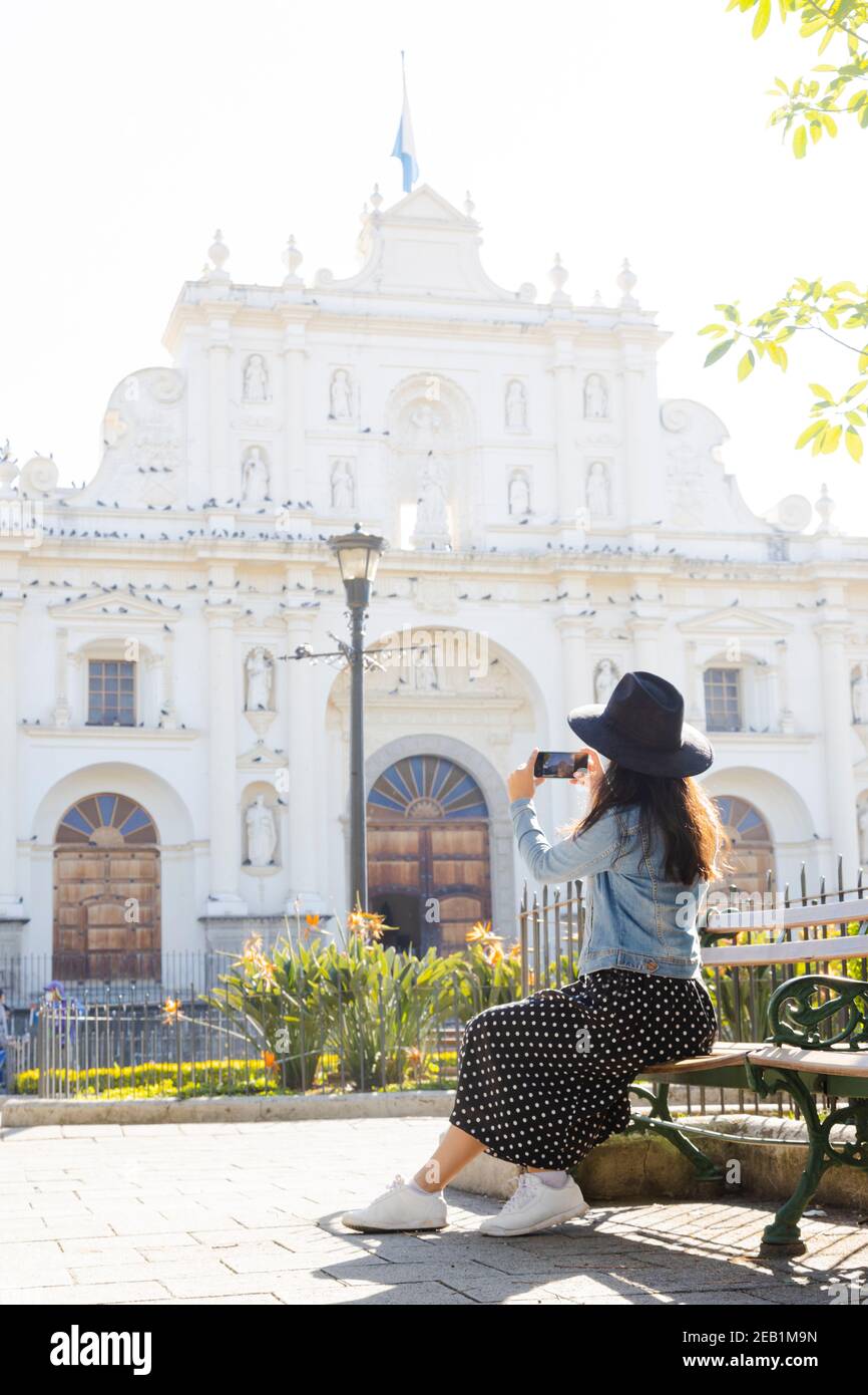 Giovane donna ispanica seduto a scattare foto alla Cattedrale di San Jose ad Antigua Guatemala-turista che documenta il suo viaggio in coloniale città-donna in th Foto Stock