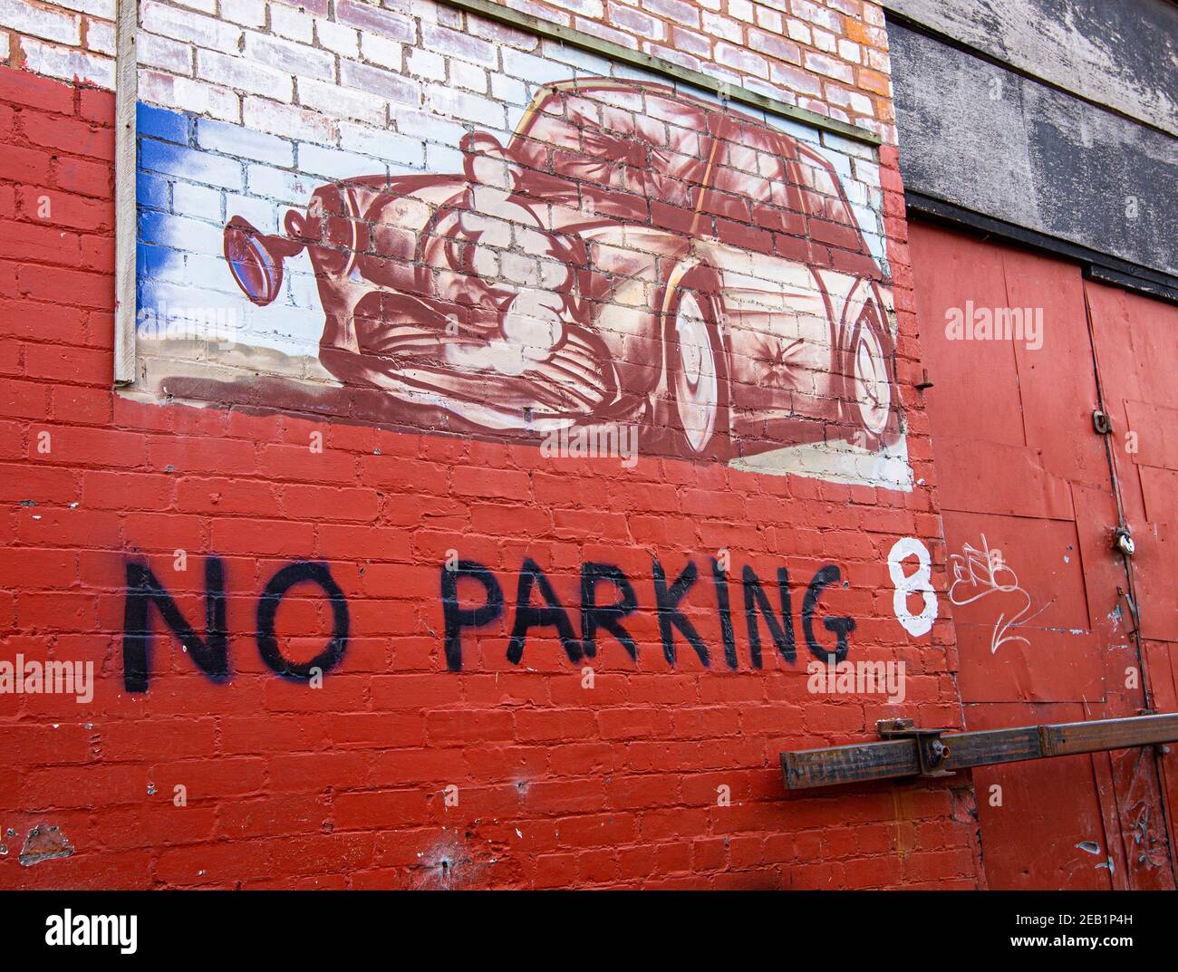 Muro dipinto di un vecchio mini schiacciato e un cartello che indica che non c'è parcheggio accanto all'ingresso di un vecchio edificio. Foto Stock