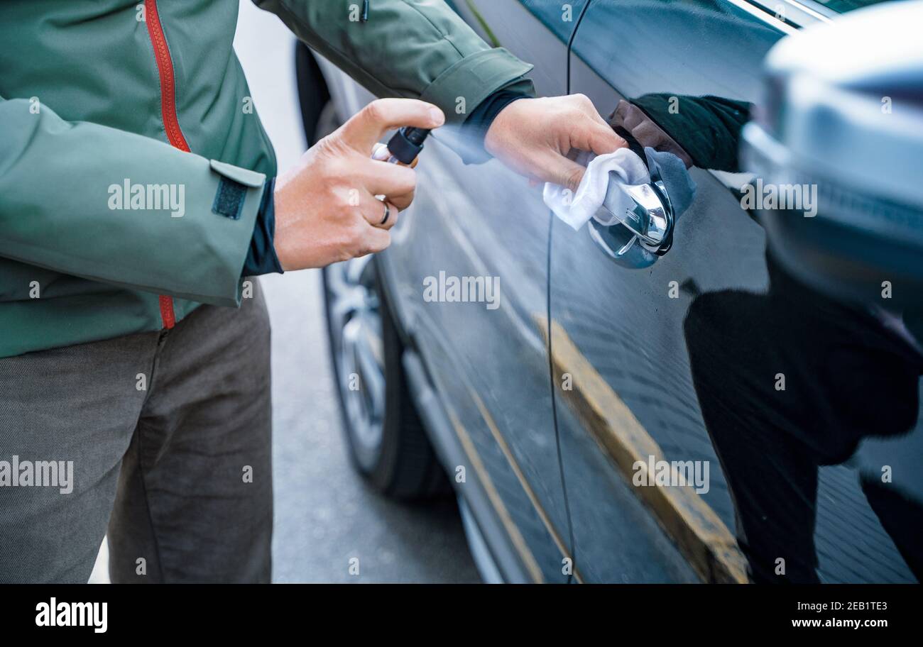 La mano dell'uomo spruzza spruzzo con disinfettante sulla maniglia della porta dell'auto, pulire le superfici pulite che vengono frequentemente toccate Foto Stock