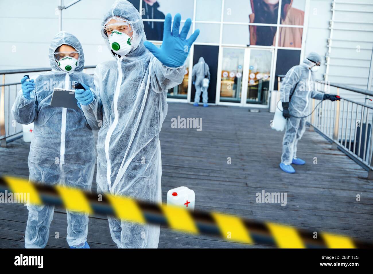 Operatore sanitario che mostra il gesto di arresto. Team di operatori sanitari che indossano tute nocciole che lavorano insieme per controllare un focolaio in città Foto Stock