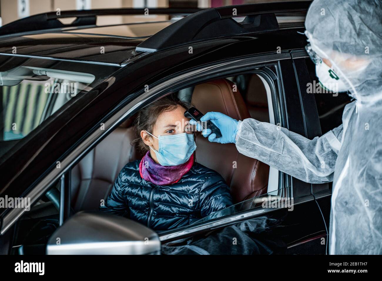 Lavoratore medico che misura la temperatura della donna attraverso il finestrino dell'auto prima di lasciare la zona di quarantena. Rimani a casa Foto Stock