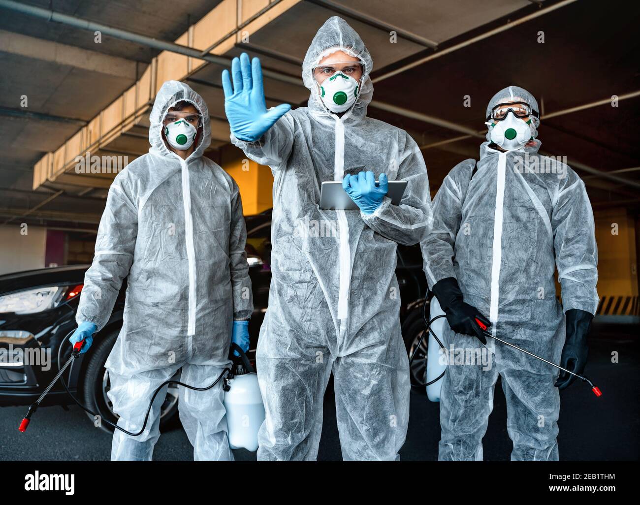 Operatore sanitario che mostra il gesto di arresto. Team di operatori sanitari che indossano tute nocciole che lavorano insieme per controllare un focolaio in città Foto Stock