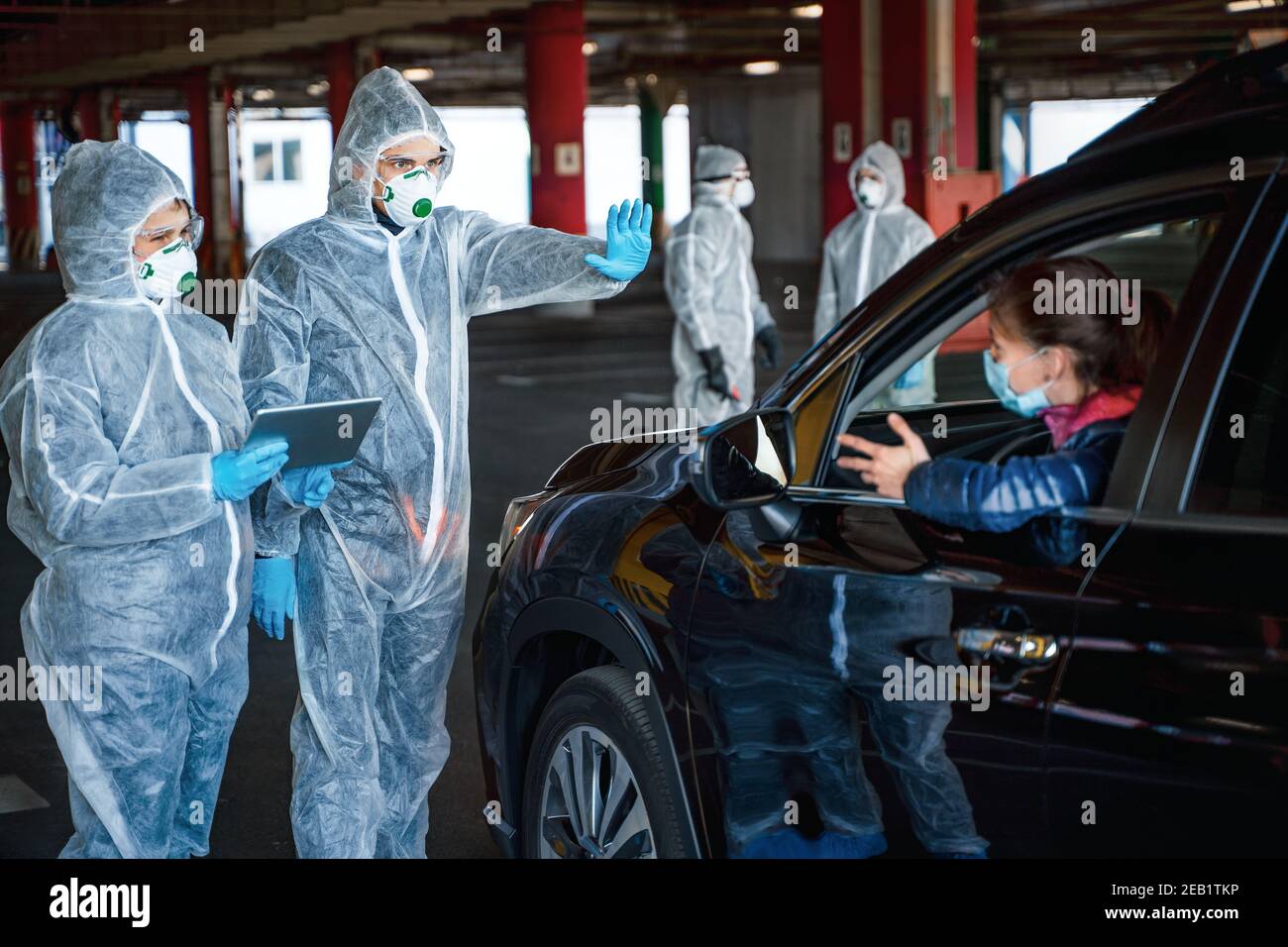 Operatore sanitario che mostra il gesto di arresto. Il team di operatori sanitari che indossano tute nocciole non lascia la zona di quarantena Foto Stock