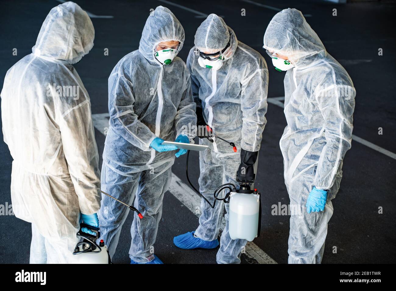 Un team di operatori sanitari che indossano tute nocciole che lavorano insieme controllare un focolaio nella città Foto Stock