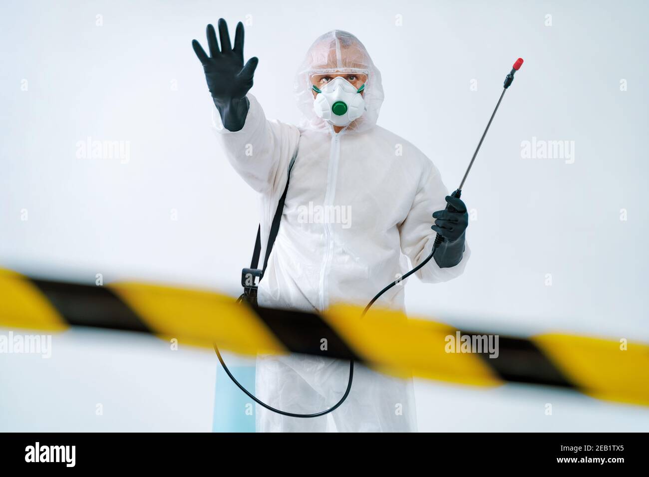 Operaio disinfettante in tuta protettiva che mostra gesto di arresto, per controllare un focolaio di virus Foto Stock