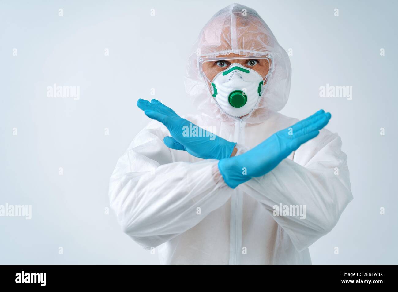 Operatore sanitario in tuta protettiva e maschera medica che mostra gesto di arresto, per controllare un focolaio di virus Foto Stock