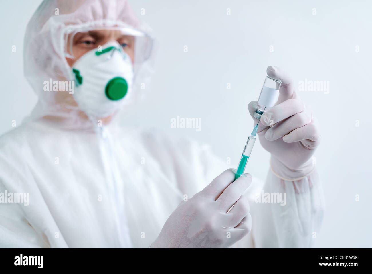 L'uomo in tuta protettiva e maschera contiene una siringa per iniezione e un vaccino. Rischio biologico. Foto Stock