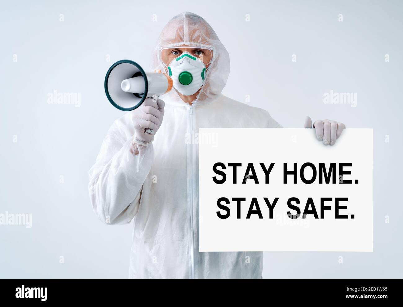 Operaio sanitario gridando nel megafono e tenendo carta con il testo 'a casa. Rimani al sicuro." in mano, proteggi dalle epidemie Foto Stock