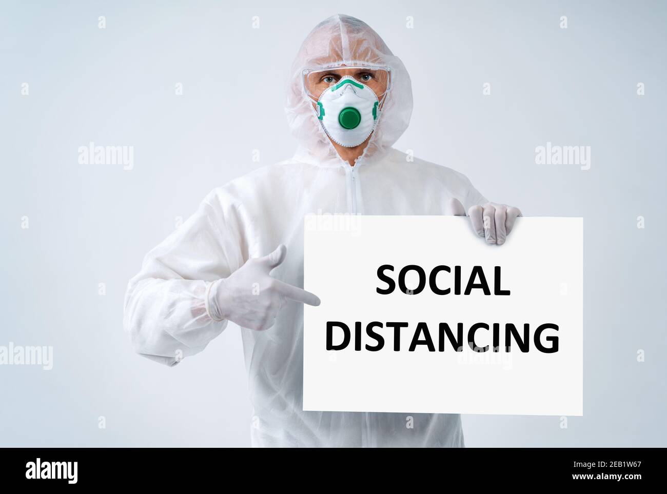Operatore sanitario in tuta protettiva e maschera medica punti su TESTO 'SOCIAL DISTANCING' Foto Stock