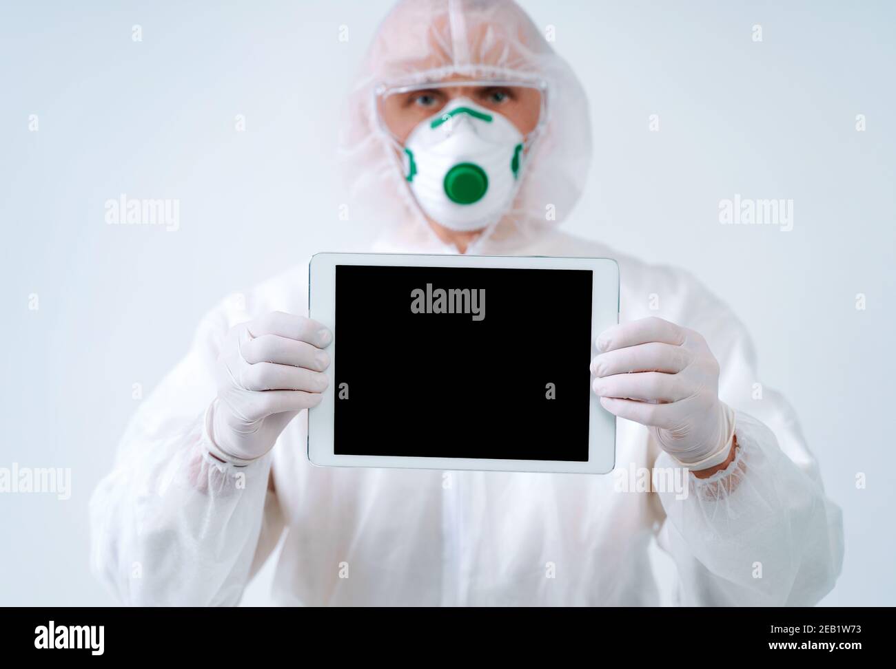 Operatore sanitario in tuta protettiva e maschera medica contiene tablet con schermo vuoto, spazio per la copia. Concetto di assistenza sanitaria. Foto Stock