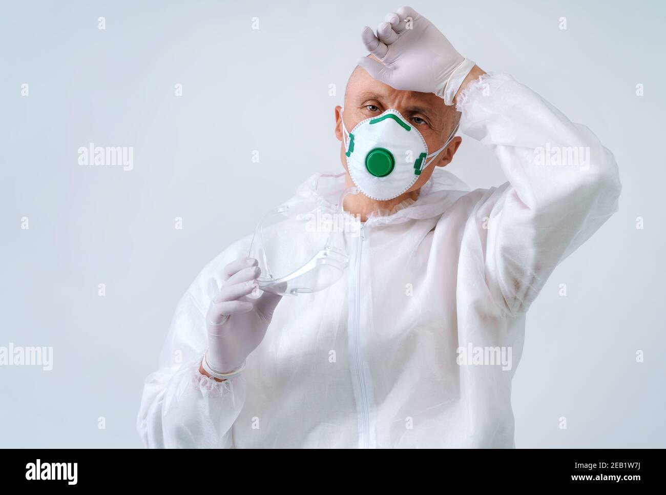 Stanco lavoratore in tuta protettiva e maschera medica su bianco sfondo Foto Stock