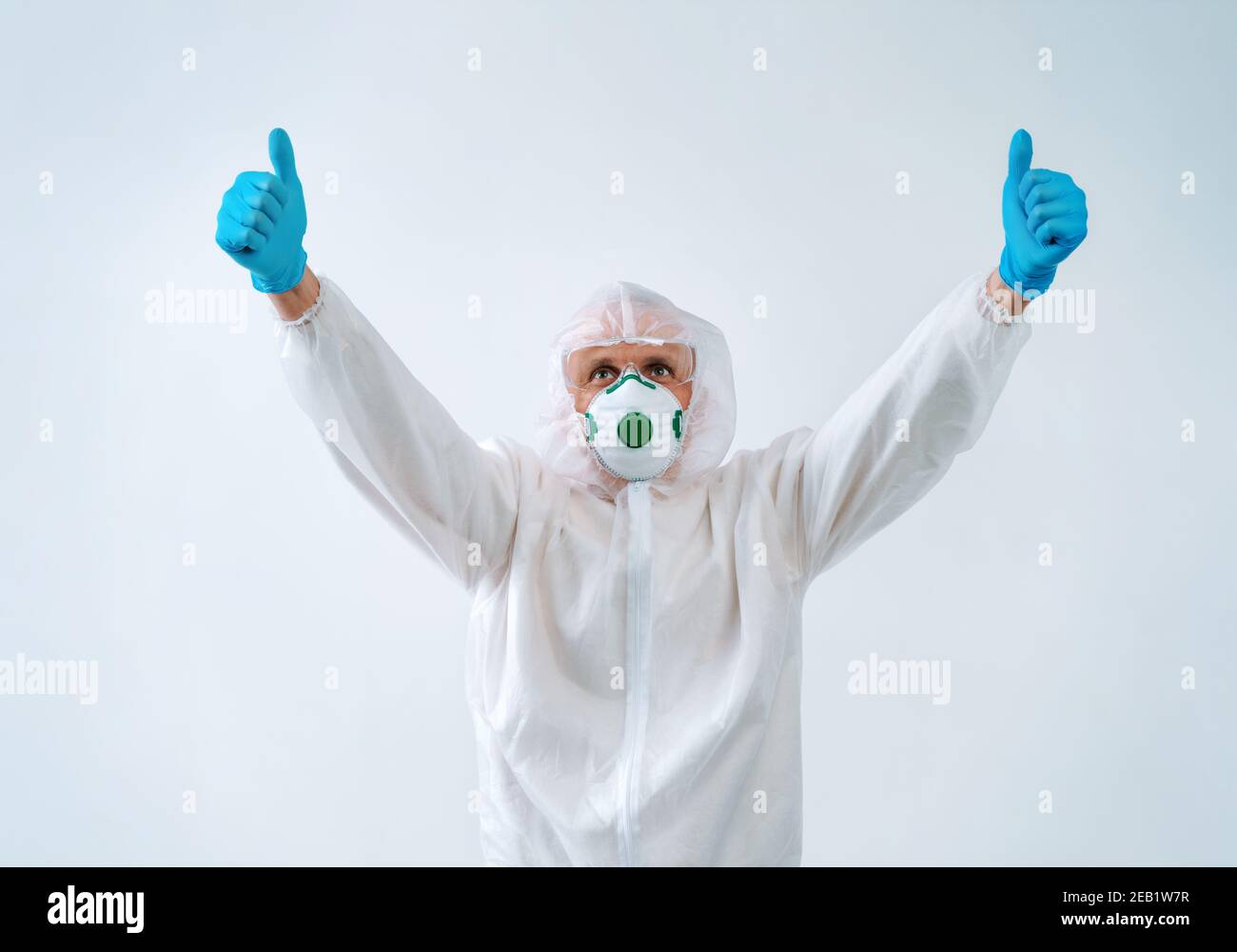 Operatore sanitario in tuta protettiva e maschera medica mostra pollici con entrambe le mani, come gesto. Foto Stock