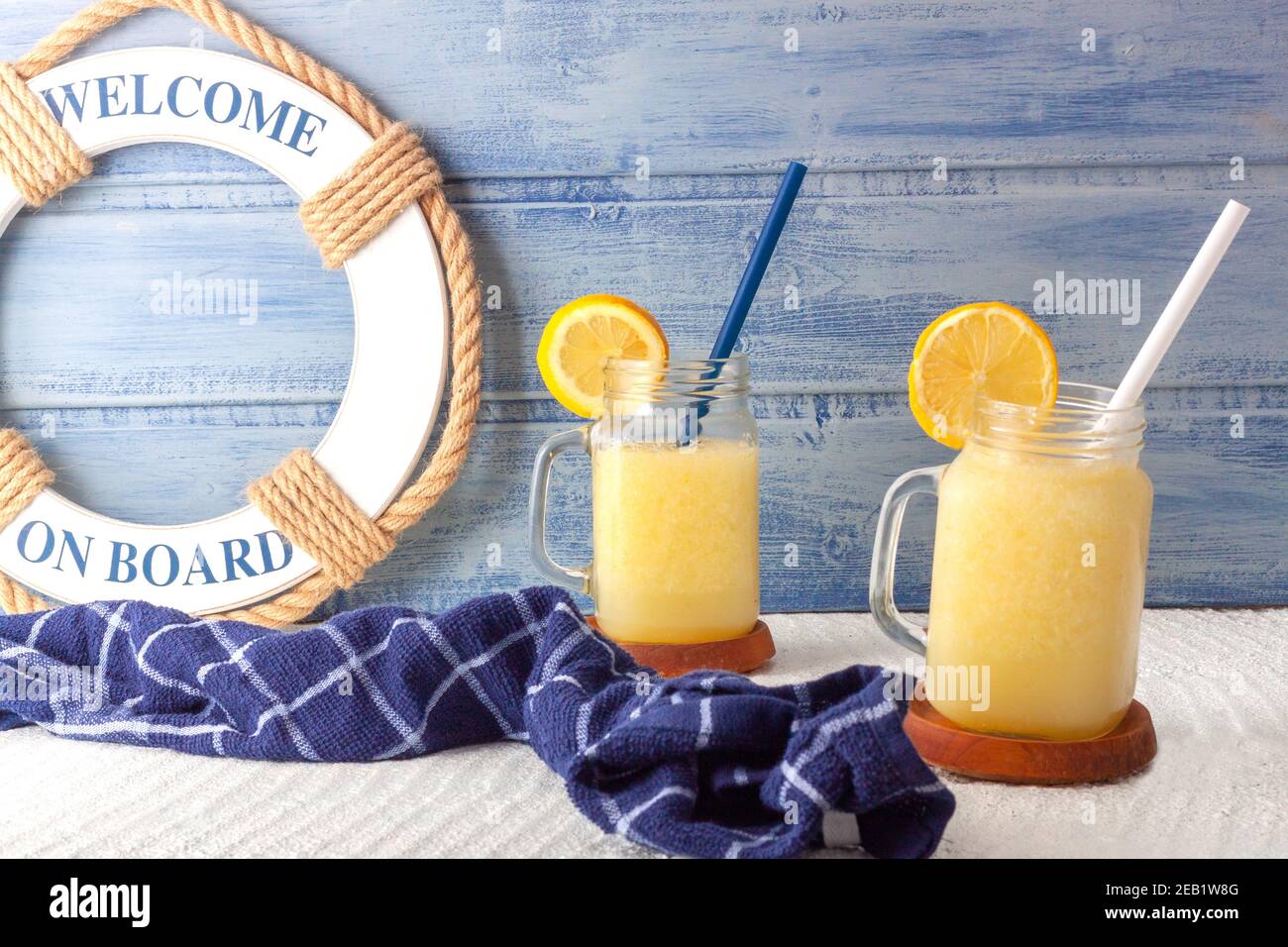 Ancora vita di due slushies limone su un tavolo bianco con uno sfondo di legno blu e un tovagliolo blu. Foto Stock